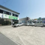Fachada da loja da Ji Consulting em Okazaki, com placa verde e estacionamento próprio